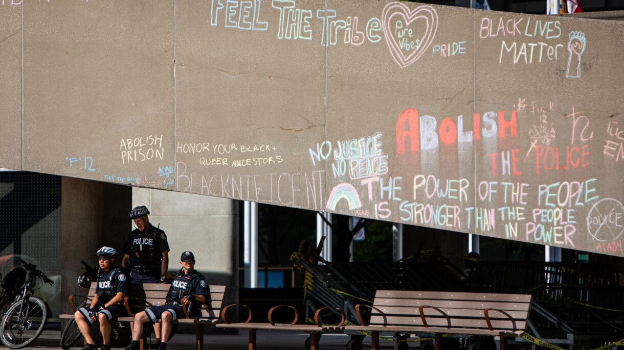 Cops sit underneath the ramp at City Hall on which in chalk is written phrases like 