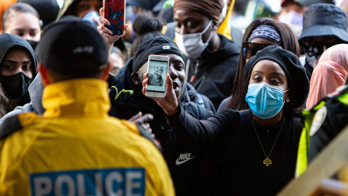 A protester holds up her phone to a police officer, showing him an image of Regis Korchinski-Paquet.