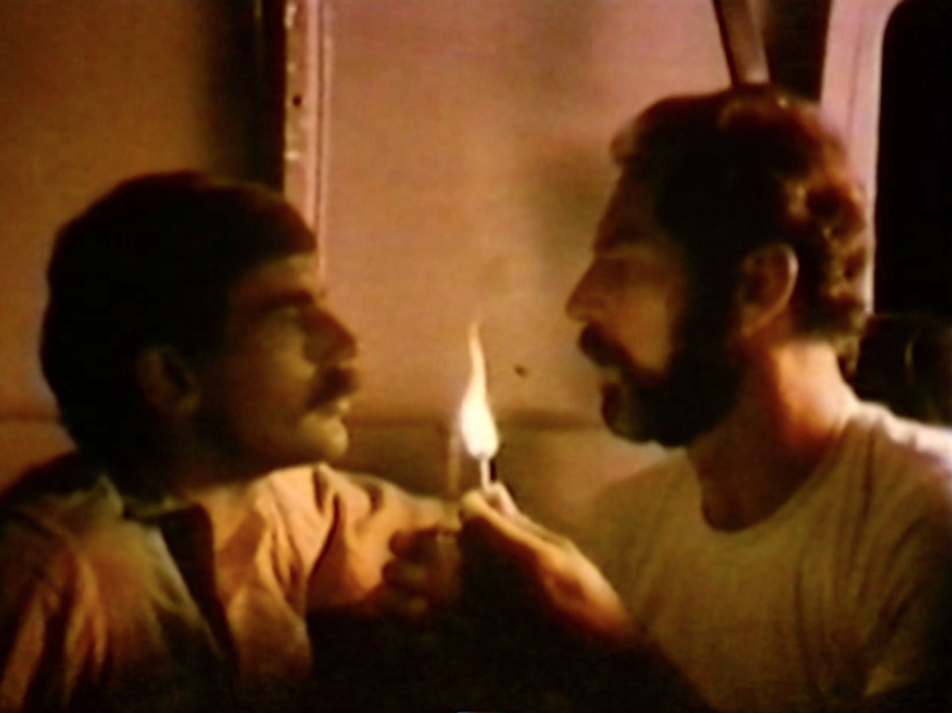 A still from 'Ask Any Buddy,' depicting two men with a flame between them.