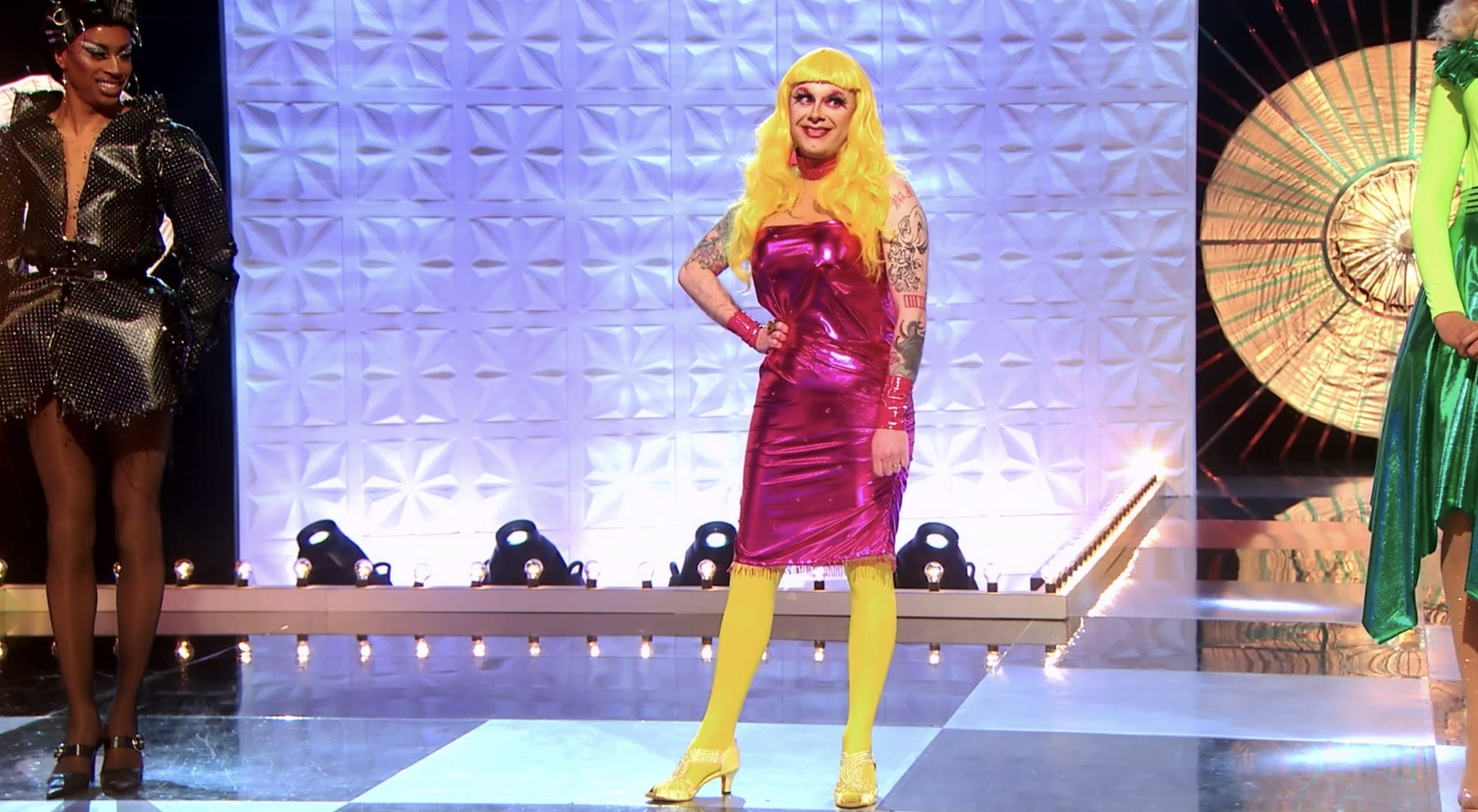 Contestant Ginny Lemon in a magenta tube dress and bright yellow wig and stockings.
