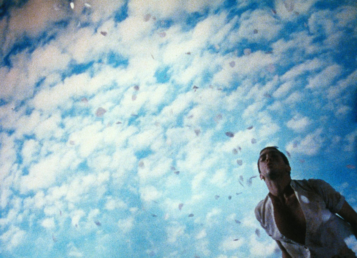 A film still showing a man standing off in the corner of the frame, most of the image is blue sky and scudding clouds.