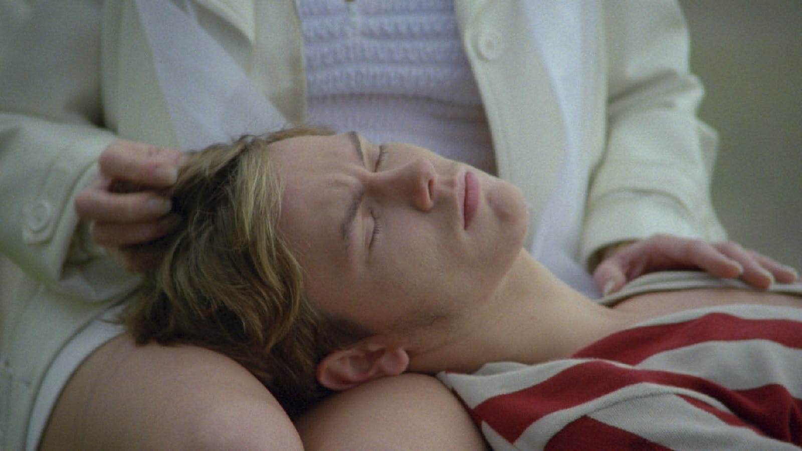 a film still of river phoenix lying unconscious, with his head resting on a woman's lap.