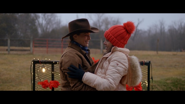 Two women, one in a western hat, the other in a toque, embrace on a farm.