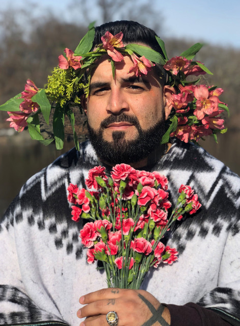 Mark Oshio is photographed holding a bouquet of flowers and a garland of flowers wrapped around his head.