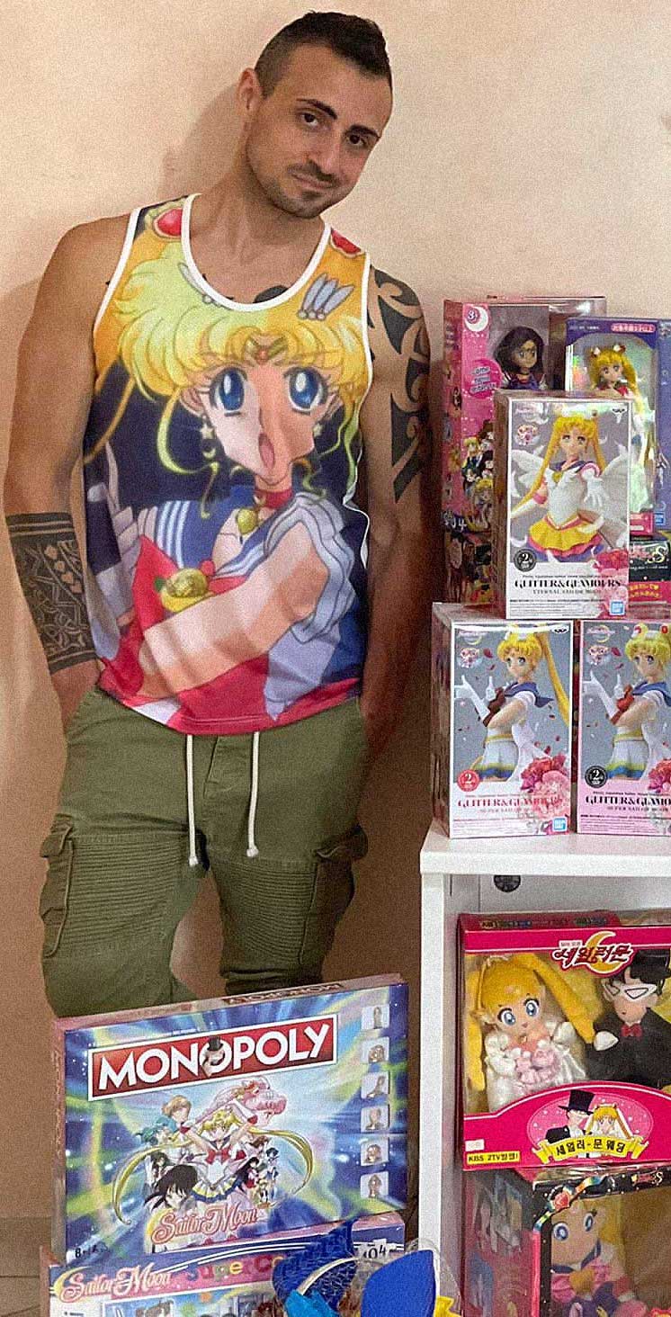 Giuseppe, in a sailor moon t-shirt, stands beside  some of his Sailor Moon collection.