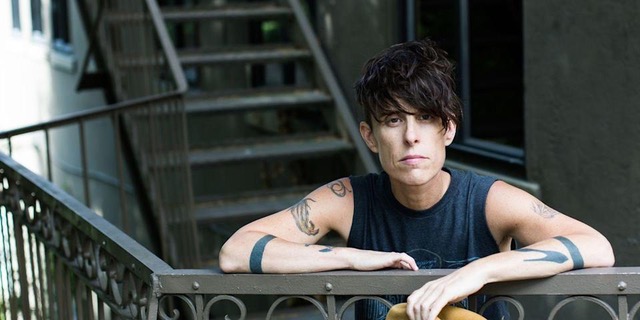 The poet is seen with tousled hair wearing a sleeveless T-shirt and leaning on a wrought iron staircase.