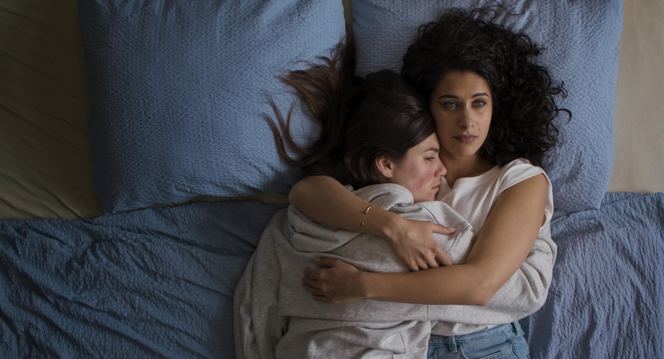 TWo women embrace in bed.