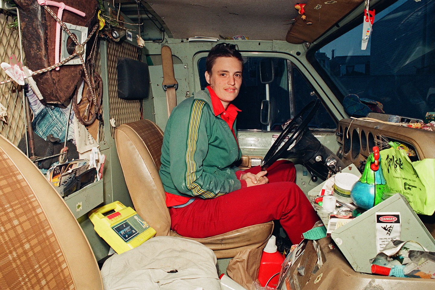A person in red and green in the cab of a messy van.
