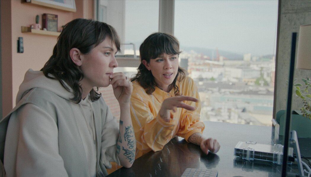 Tegan and Sarah face a computer screen and appear to be engaged in conversation.