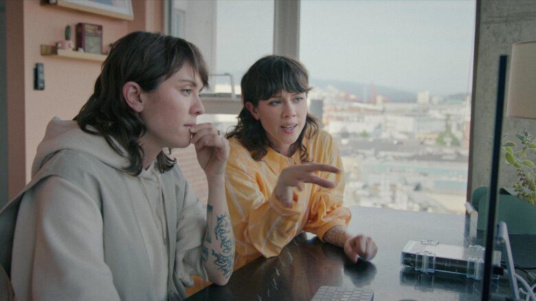 Tegan and Sarah face a computer screen and appear to be engaged in conversation.