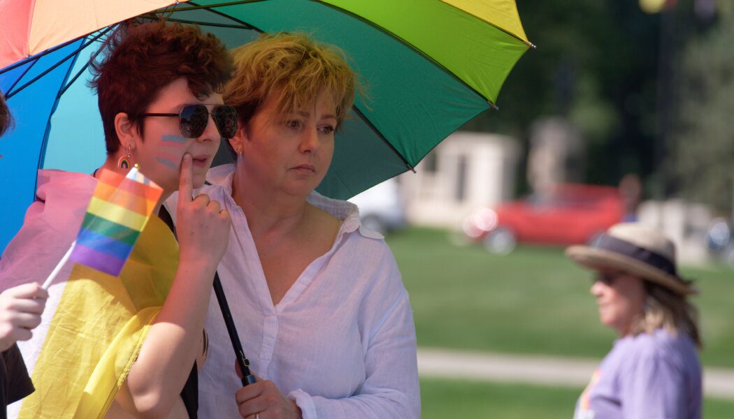 Two people attend a protest in Regina, Sask., in reaction to a policy that says schools in the province must seek parental or guardian permission when changing the name and pronouns used by queer and trans students younger than 16.