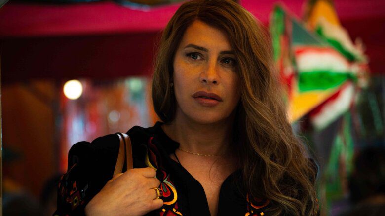 Karla Sofía Gascón as Emilia Perez in Emilia Perez. Gascón wears black with colourful embroidery, has long hair, and a brown purse and delicate chain.