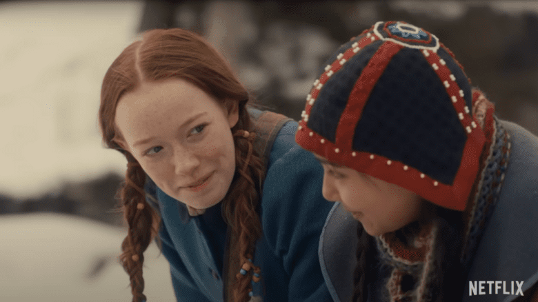 A still image of Anne, played by Amybeth McNulty, in braids and a coat, looking at another child in Anne with an E.