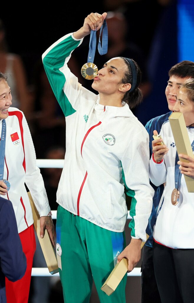 Silver Medallist Liu Yang of Team People's Republic of China (L), Bronze Medallist Janjaem Suwannapheng of Team Thailand (obscured) and Bronze Medallist Nien Chin Chen of Team Chinese Taipei (R) react as Gold Medallist Imane Khelif of Team Algeria (C) kisses her medal. Khelif wears green and white.