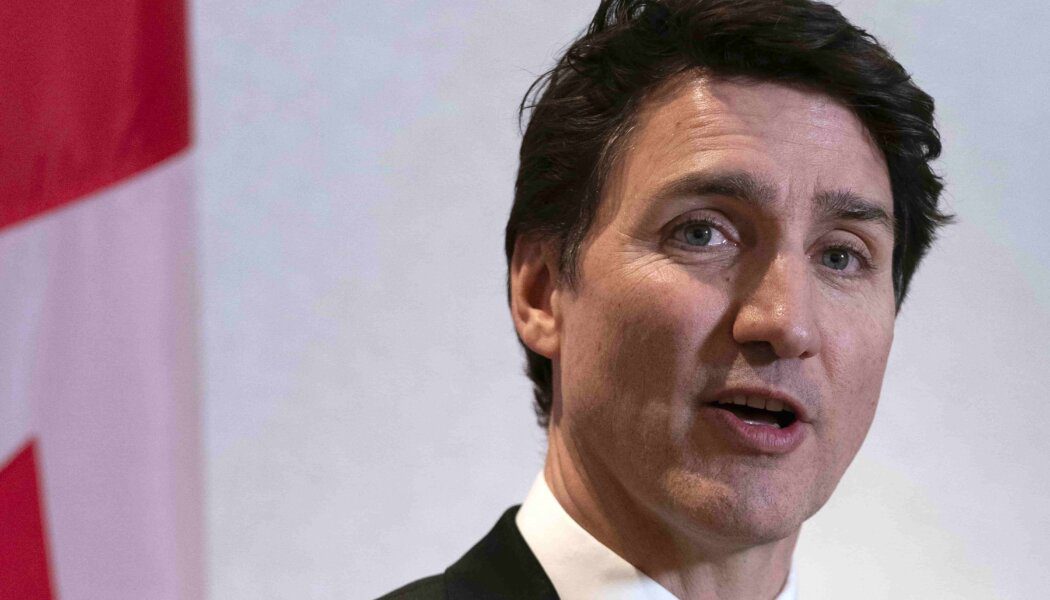 Prime Minister Justin Trudeau wears a suit and tie; he speaks in front of a Canadian flag.