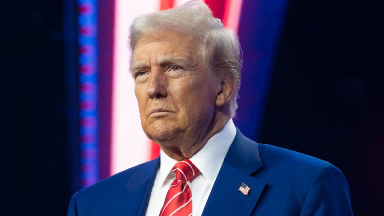 Donald Trump wears red, white and blue; he is frowning.