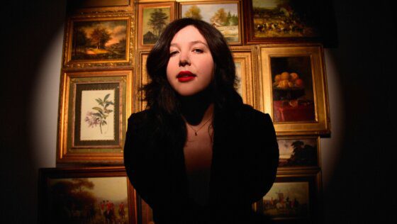 Lucy Dacus in front of numerous paintings.