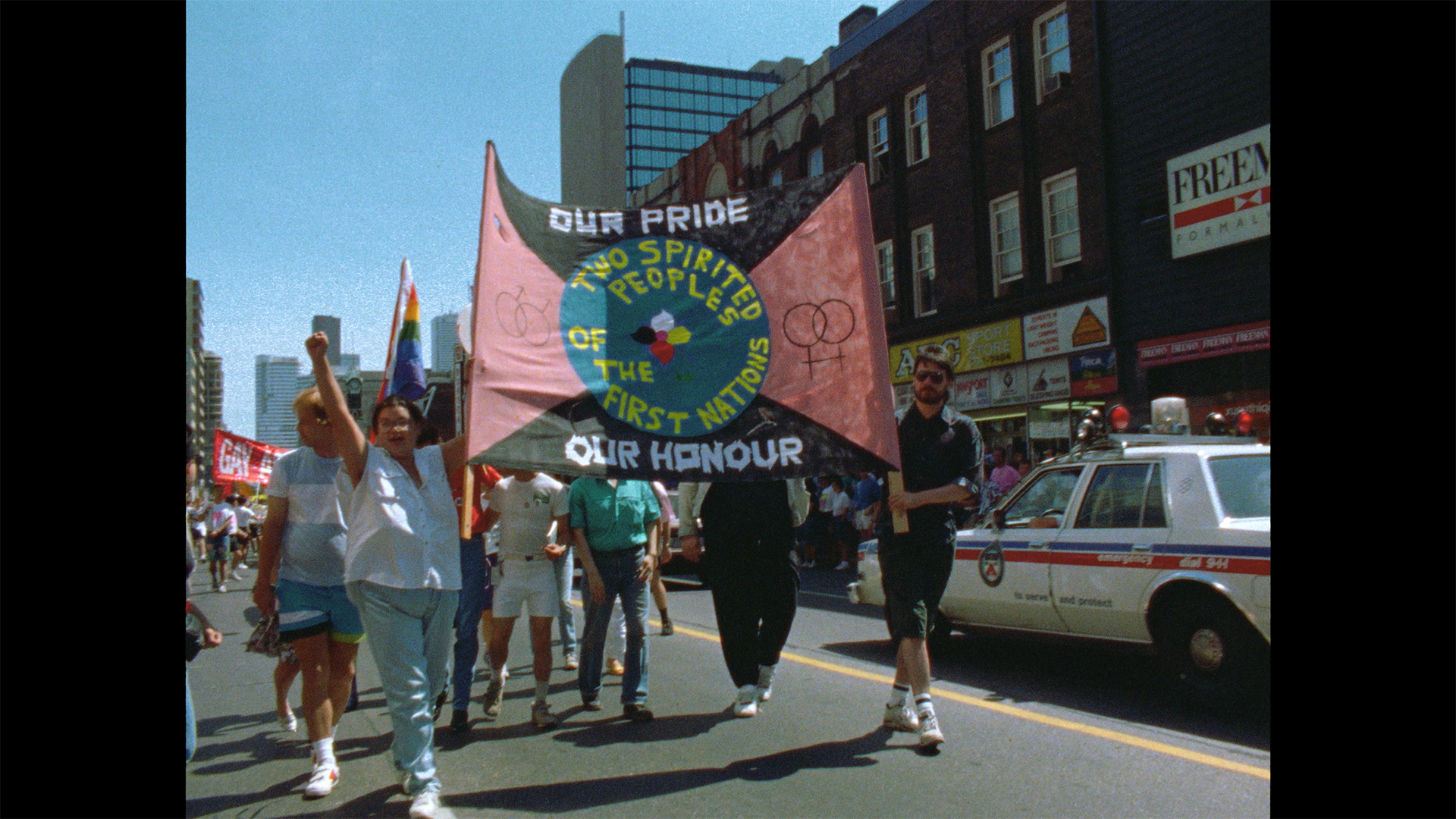 People march on a Toronto street with a sign that says "Our Pride, Our Honour" and "Two-Spirited Peoples of the First Nations.