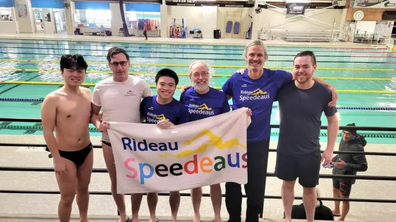 Six members of the Rideau Speedeaus hold a sign with the league's name on it in front of a pool