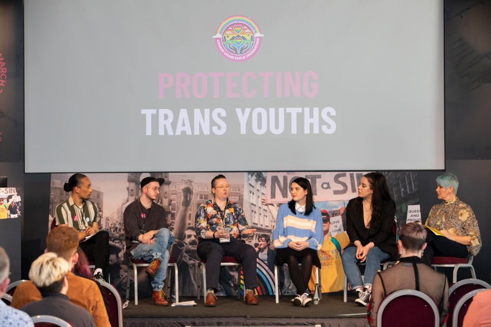 Six people on a panel discussion under a screen that reads "PROTECTING TRANS YOUTHS"
