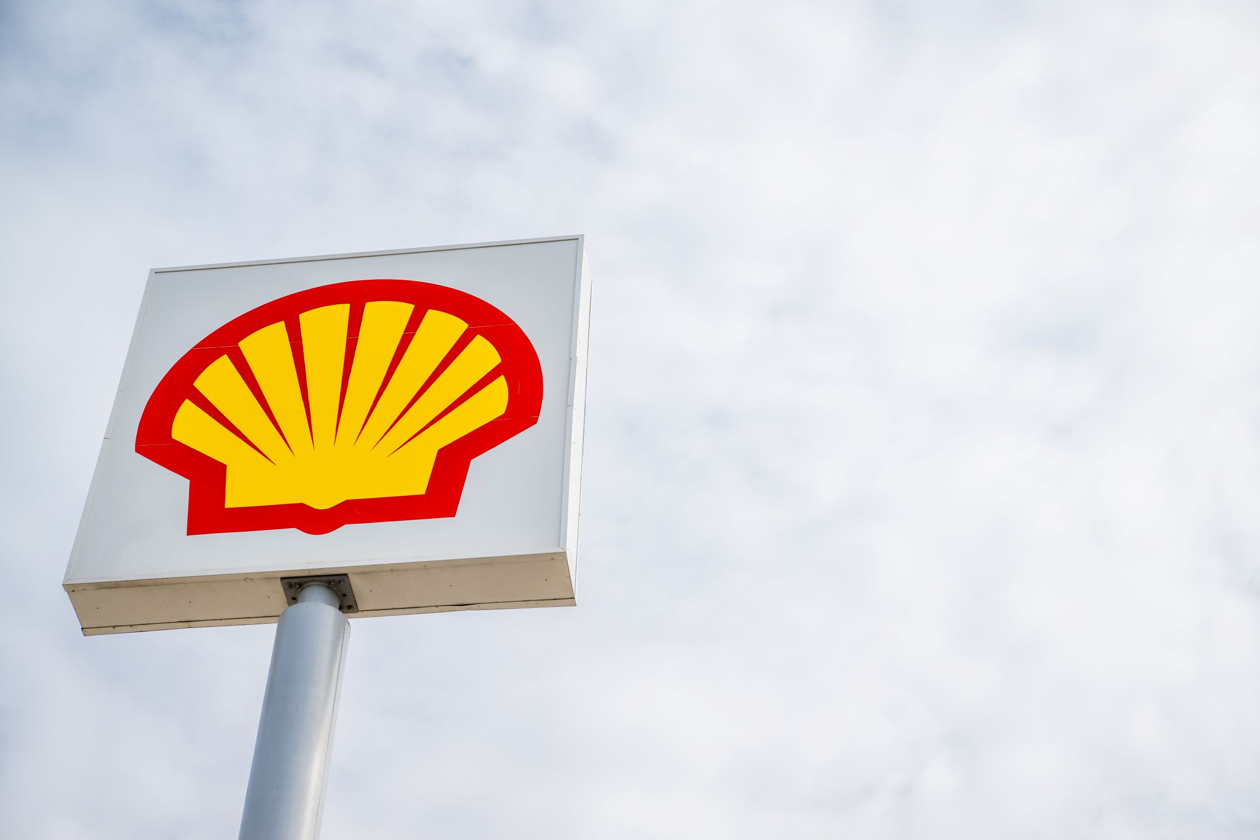 The Shell gas station logo against a cloudy sky representing the fossil fuel industry.