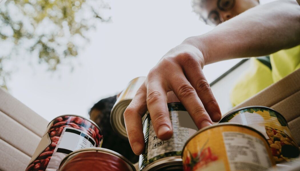 Photo of a person reaching into a box to grab a can of food from a stack