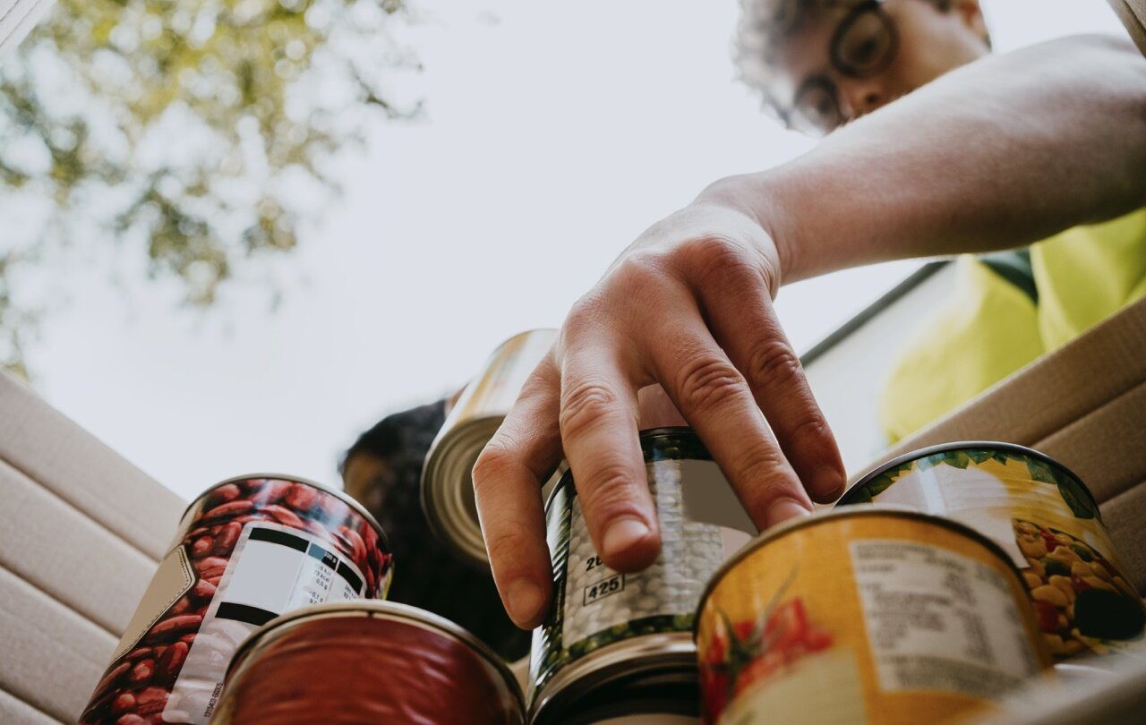 Photo of a person reaching into a box to grab a can of food from a stack