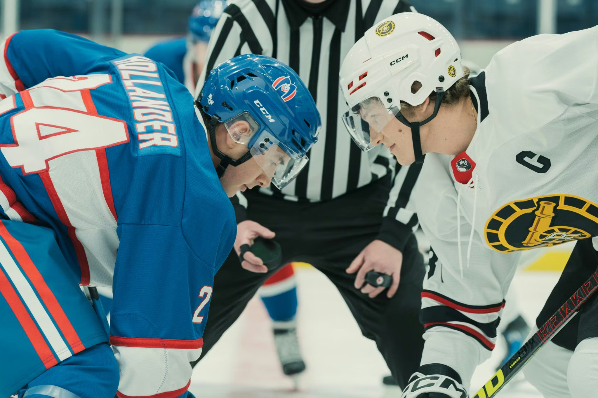 Two hockey players face off; one is wearing a white uniform and helmet, the other blue.