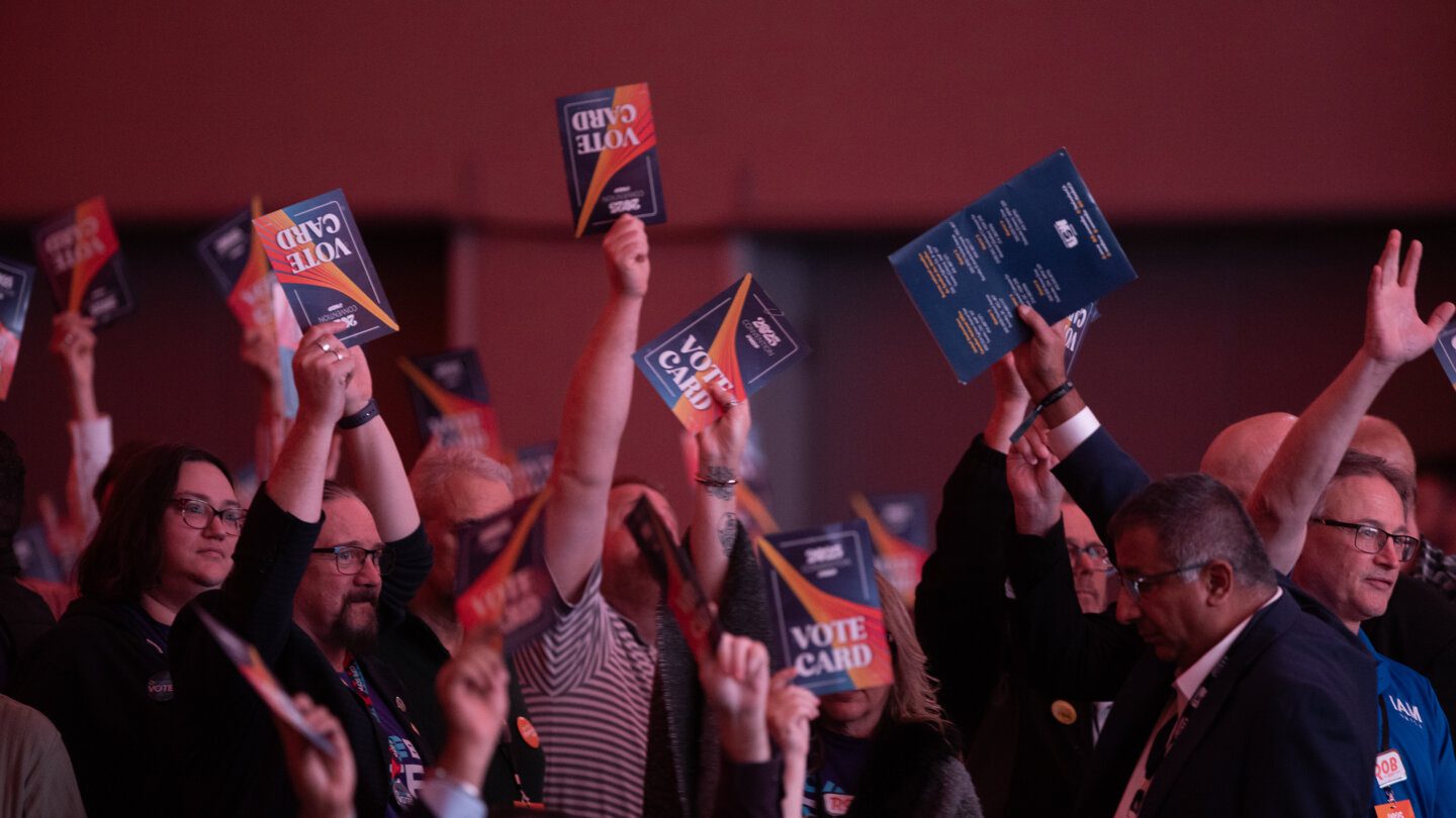 A crowd of people raising paper slips labelled "Vote Card" in the air