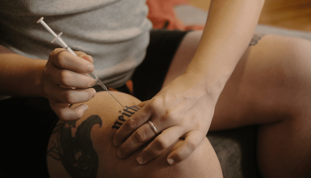 A nonbinary person injects hormones with a syringe