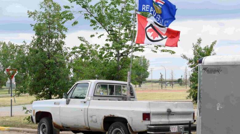 A white pickup truck flies a modified Alberta provincial flag with the word Republic added and an upside down Canadian flag with a No symbol on it is pictured in Oyen, Alberta on June 20, 2025. A decal on the back window depicts a figure urinating on a Quebec symbol and the word Frogs.