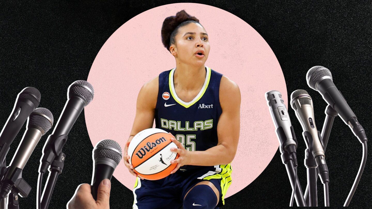 WNBA player Azzi Fudd wears a jersey that says 35/Dallas. She holds a basketball. Many microphones are pointed at her.