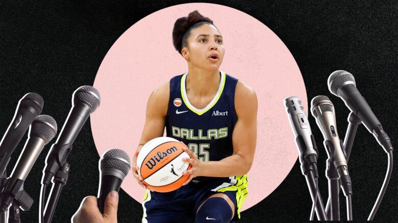 WNBA player Azzi Fudd wears a jersey that says 35/Dallas. She holds a basketball. Many microphones are pointed at her.