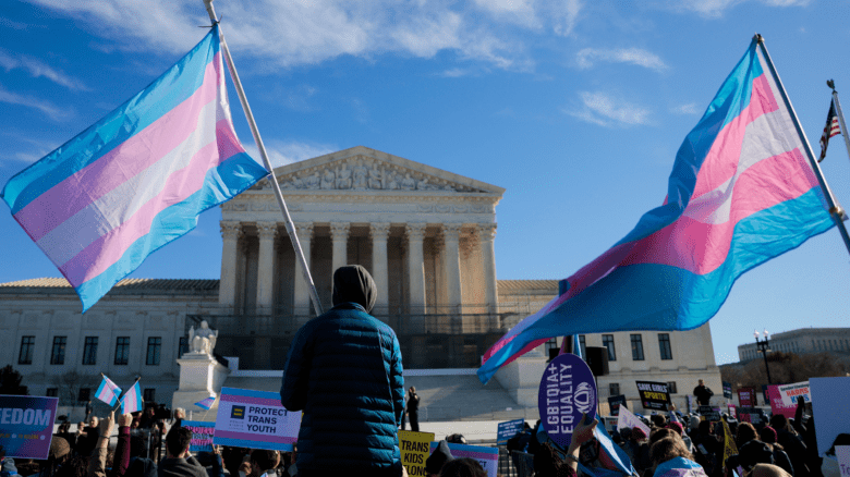 A trans flag is waved in front of the U.S. Supreme Court