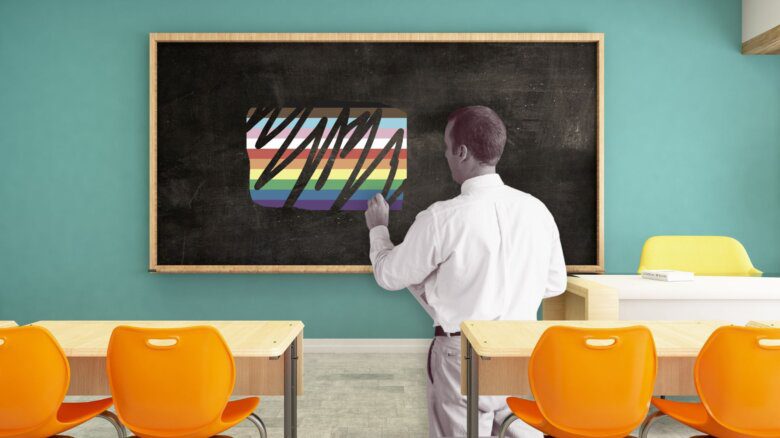 A teacher standing at a blackboard that has a Pride flag scribbled out on it