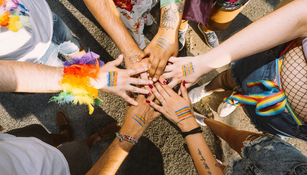 People from varuous backgrounds come together to celebrate queer and trans inclusivity by offering their hands into a united circle.